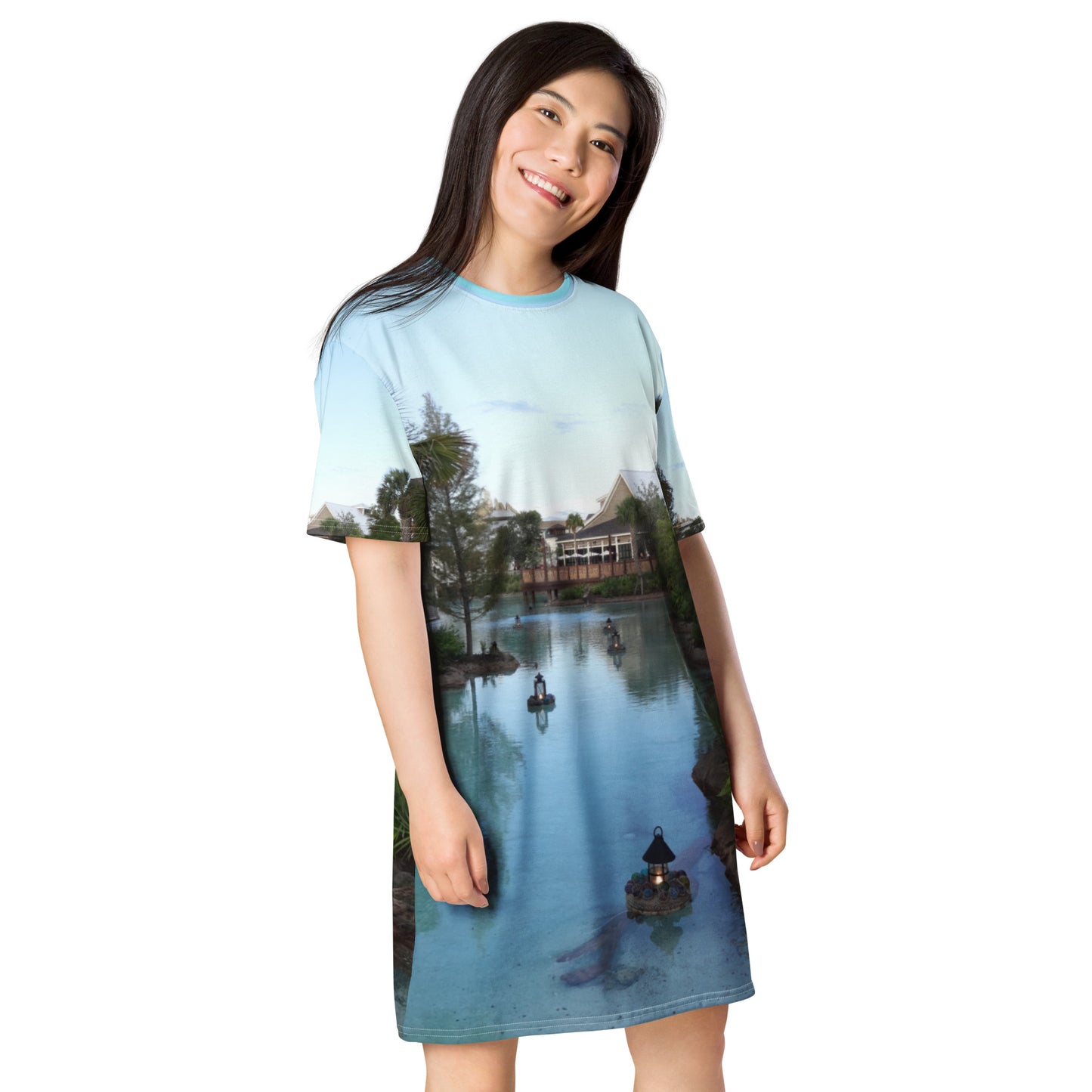Pictured is a women wearing an all over print tshirt dress with a photograph of a little river flowing through a village - right front