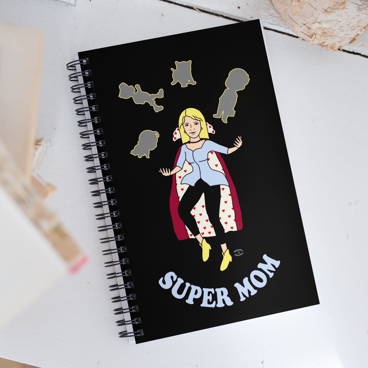 A Picture of a spiral notebook cover and on the front a picture with the image is of a mother in a cape juggling her family with the text at the bottom Super Mom