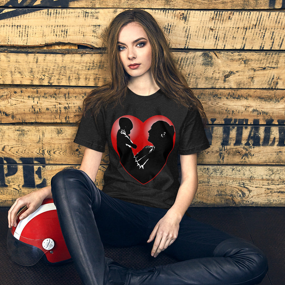 A women sitting against a wall wearing a short sleeve tshirt with a picture on the front of a mother holding up a baby in silhouette with white light shining from behind and a red love heart framing them - Front - black