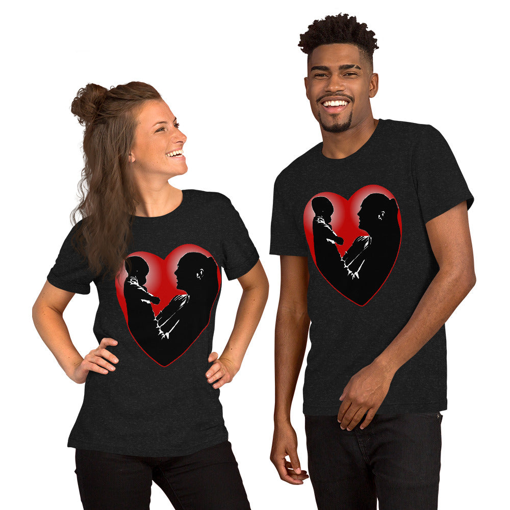 A man and a women wearing matching short sleeve tshirt with a picture on the front of a mother holding up a baby in silhouette with white light shining from behind and a red love heart framing them - Front - black heather