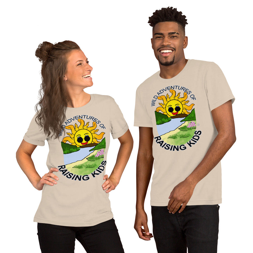 A man and a woman wearing matching tshirts with a picture of the sun coming up over the mountains with sunglasses on and a little stream gently flowing trees and bushes can be seen on the closer mountains and a small beach with some flowers are on the closes bank around the outside of the picture is written "Wild Adventures of Raising Kids" unisex tshirt - soft cream front